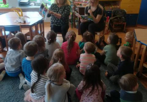 Dzieci siedzą na dywanie, panie czytają im książkę o przygodach Koziołka Matołka